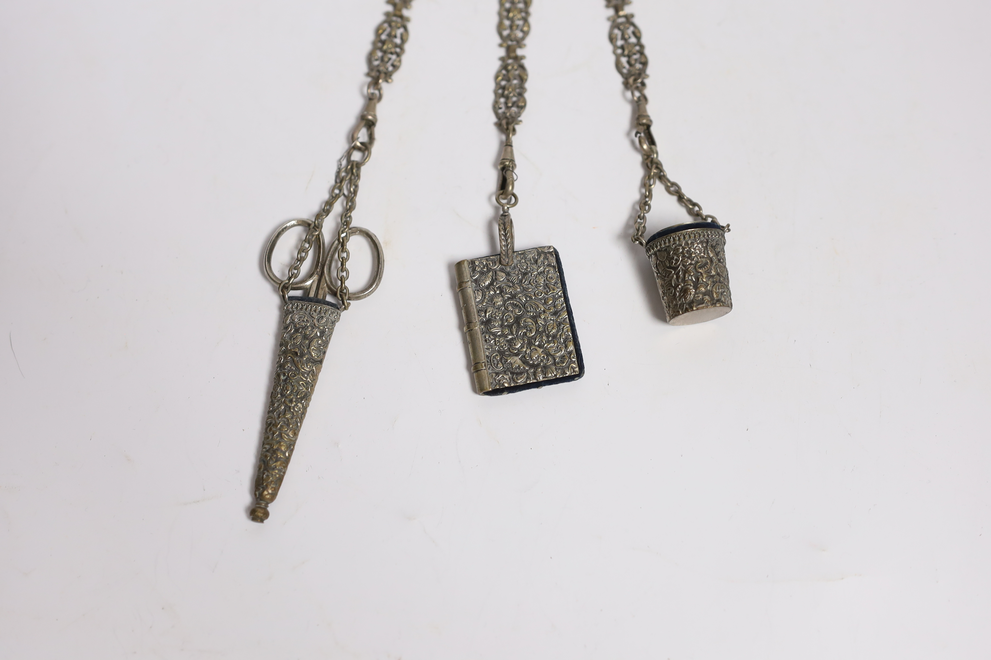 A late 19th century pierced silver plated chatelaine, hung with three accoutrements, to include a cased pair of scissors, pin cushion and thimble holder, overall 29.5cm.